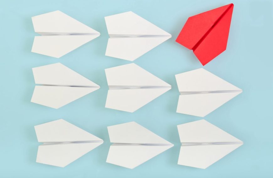 A group of paper airplanes with a red one in the middle.
