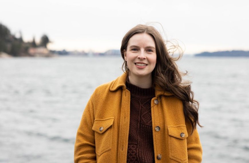 A young woman in a yellow coat standing in front of a body of water.