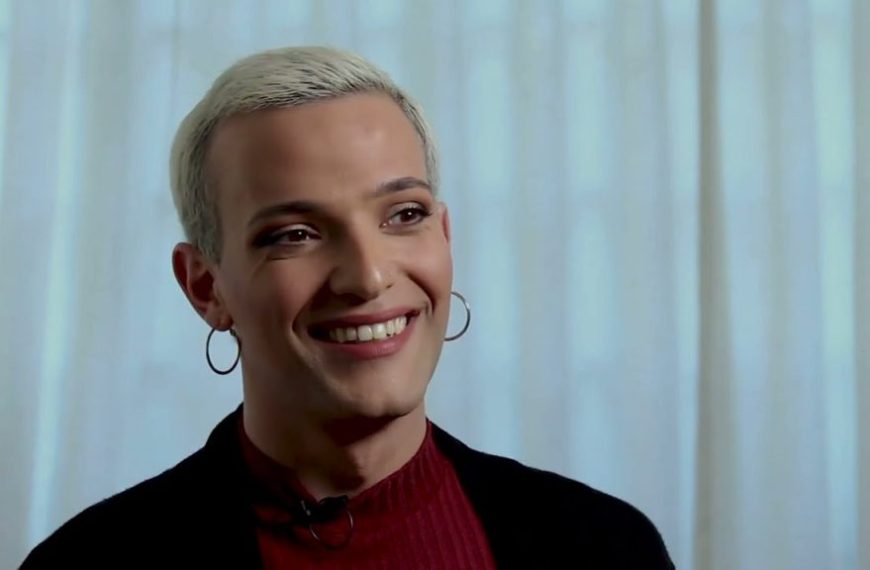 A woman with white hair smiling in front of a curtain.