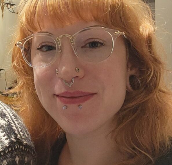 A woman with red hair and glasses is posing for a photo.