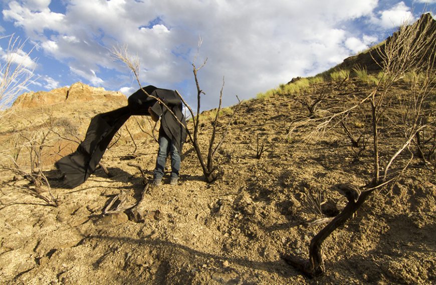 A person standing on a hill with a black cloth over his head.