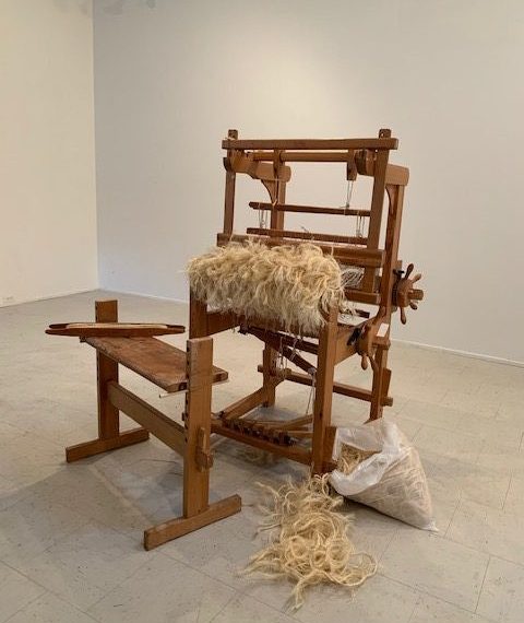 A wooden loom is sitting on a table in an empty room.