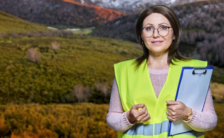 A woman holding a clipboard in front of a mountain.