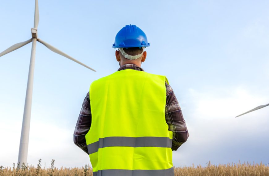 A man in a hard hat is standing in front of wind turbines.