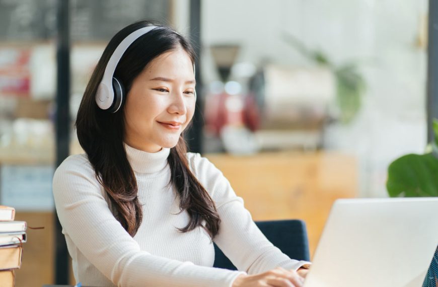 A young asian woman using a laptop with headphones.