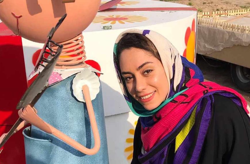A woman wearing a scarf is standing next to a doll.