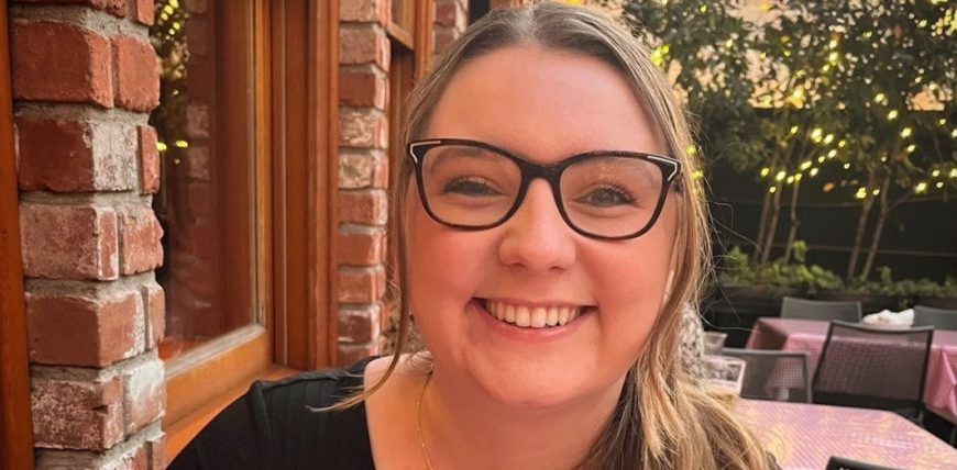 A woman with glasses smiling at an outdoor table.