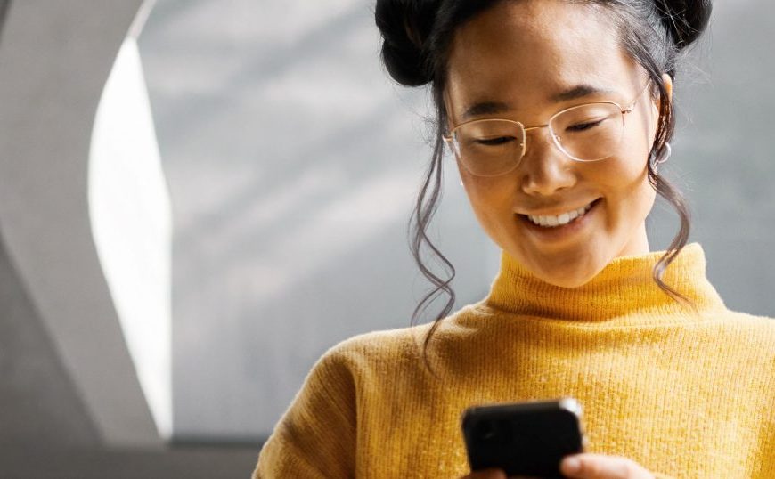 A woman wearing glasses is looking at her phone.
