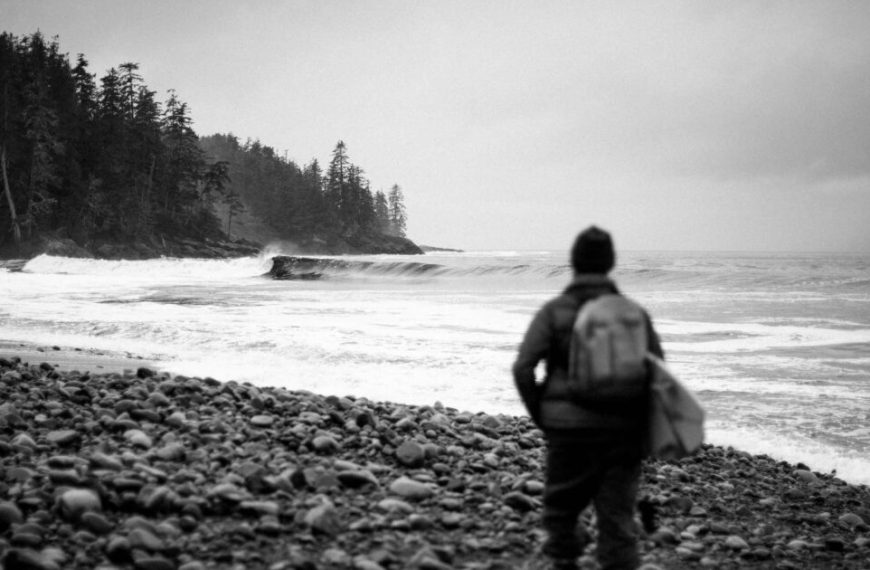 A black and white photo of a person standing on a rocky beach.