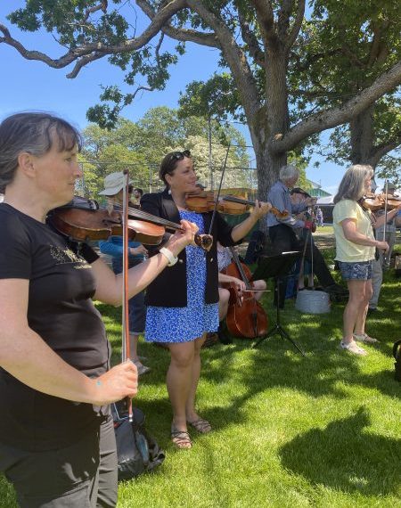 A group of people playing violins in a grassy area.