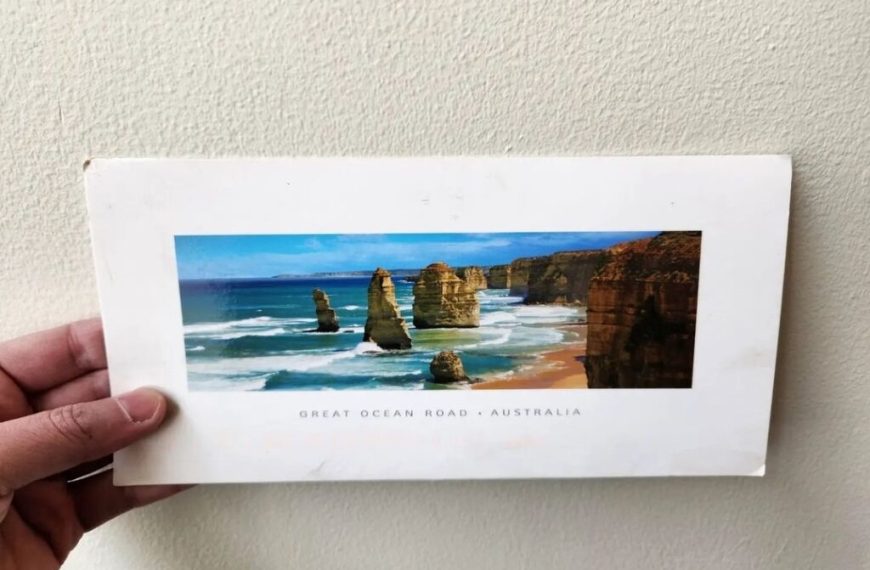 A hand holding a postcard of the great ocean road.