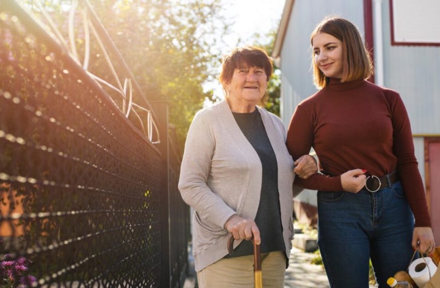An older woman and a younger woman walking in front of a fence.