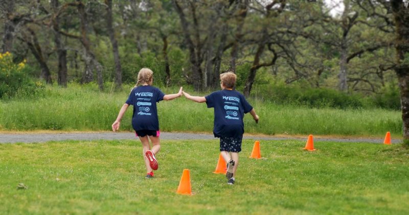Two children running through orange cones on a grassy field.