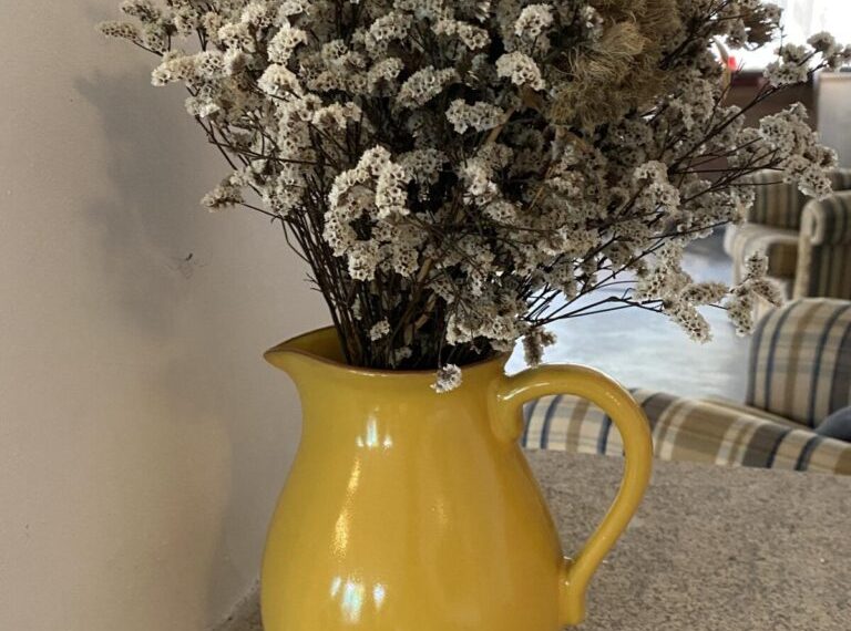 A yellow pitcher with dried flowers in it.