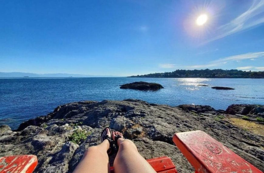 A woman sits on a red bench overlooking the ocean.