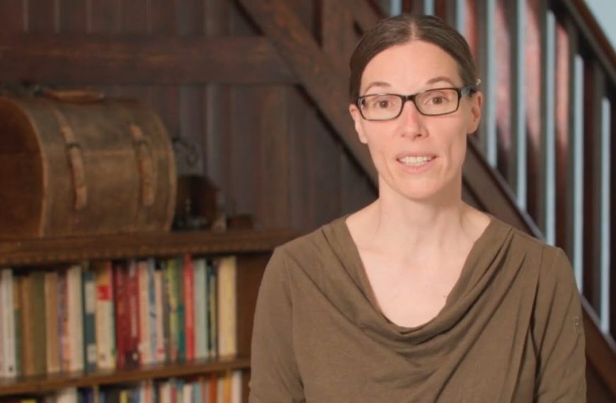 A woman in glasses standing in front of a bookcase.