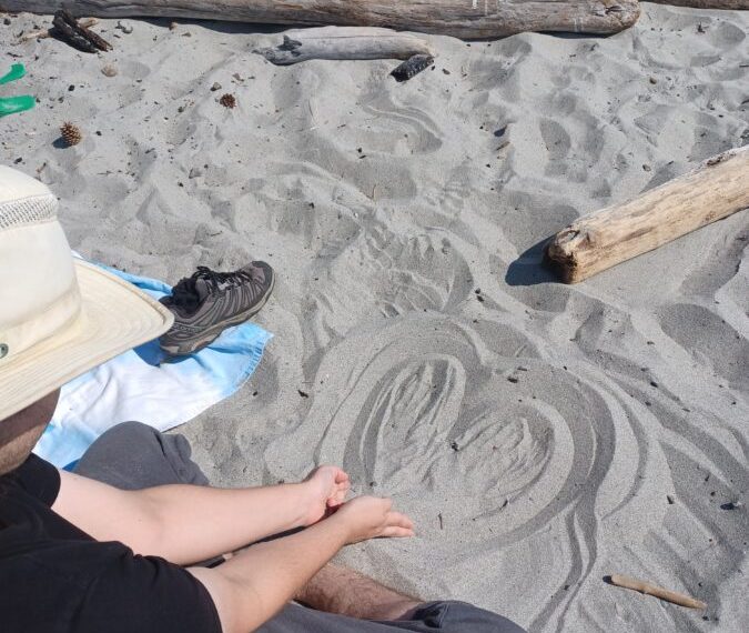 A person sitting on the beach with a hat and drawing in the sand.