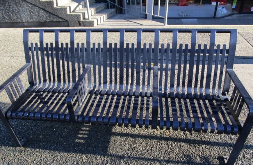 A black bench is sitting on a sidewalk in front of a building.