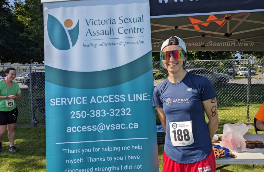 A woman standing next to a banner for the victoria sexual assault centre.