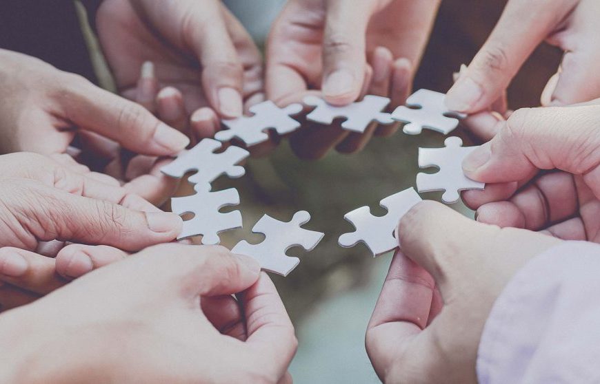 A group of people holding jigsaw puzzle pieces together.