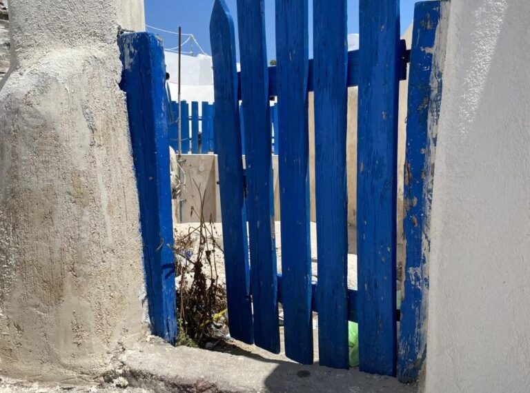 A blue wooden gate in front of a white building.