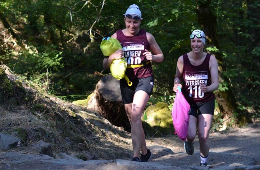 Two men are running down a trail in the woods.