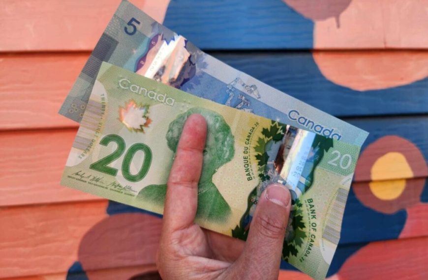 A person holding two canadian dollars in front of a colorful wall.