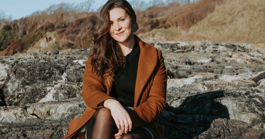 A woman in a brown coat sitting on rocks.