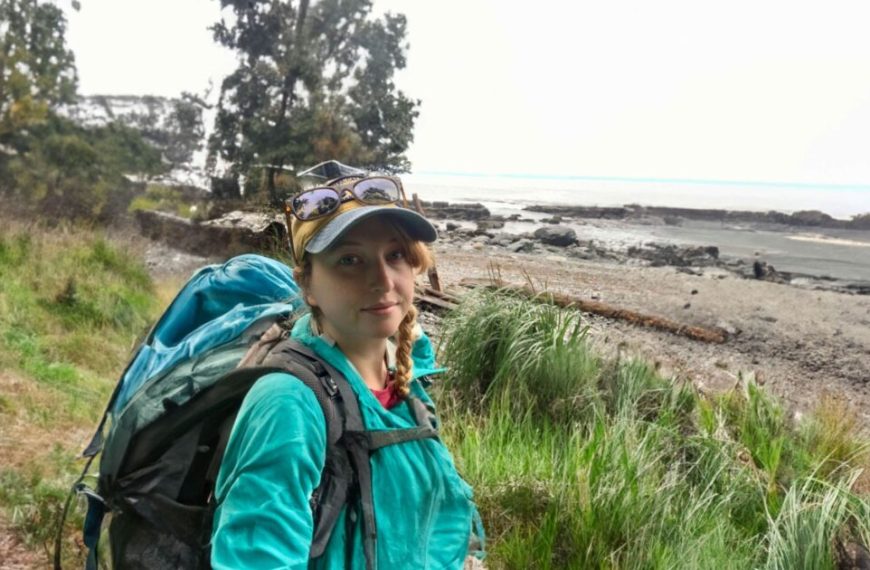 A woman with a backpack on a trail near the ocean.