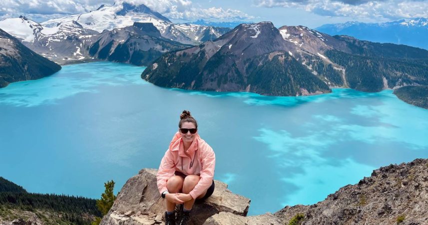 A woman sitting on top of a mountain overlooking a blue lake.