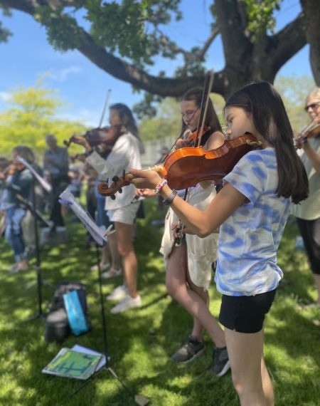 A group of people playing violin in a park.