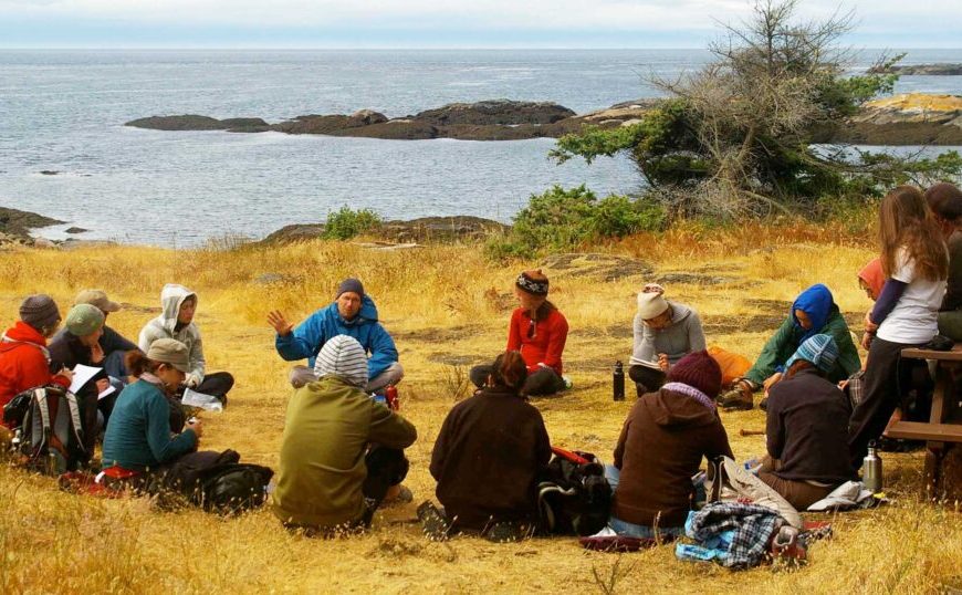 A group of people sitting in a circle near the ocean.