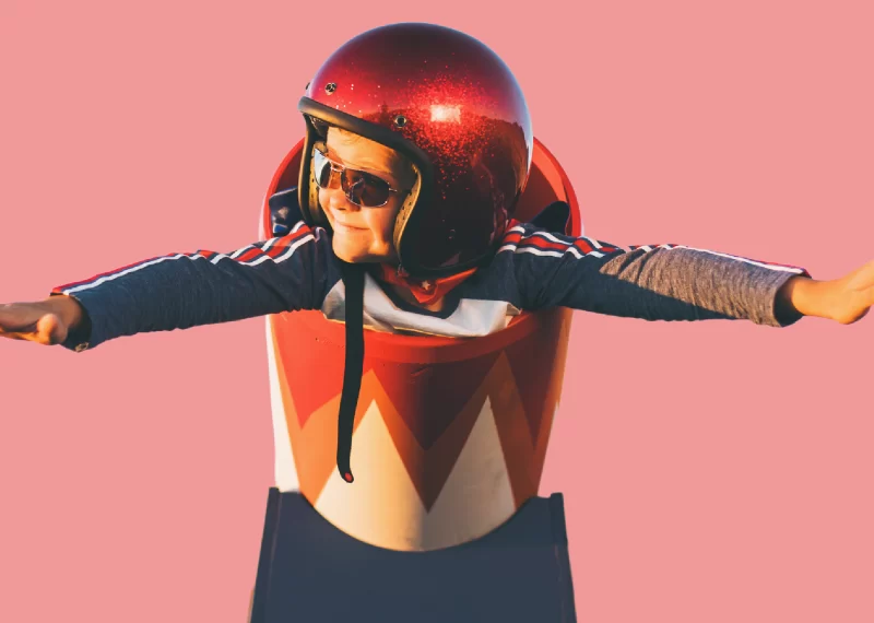 A child wearing a helmet and riding a bike on a pink background.