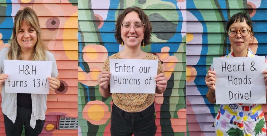 Four women holding signs in front of a colorful wall.