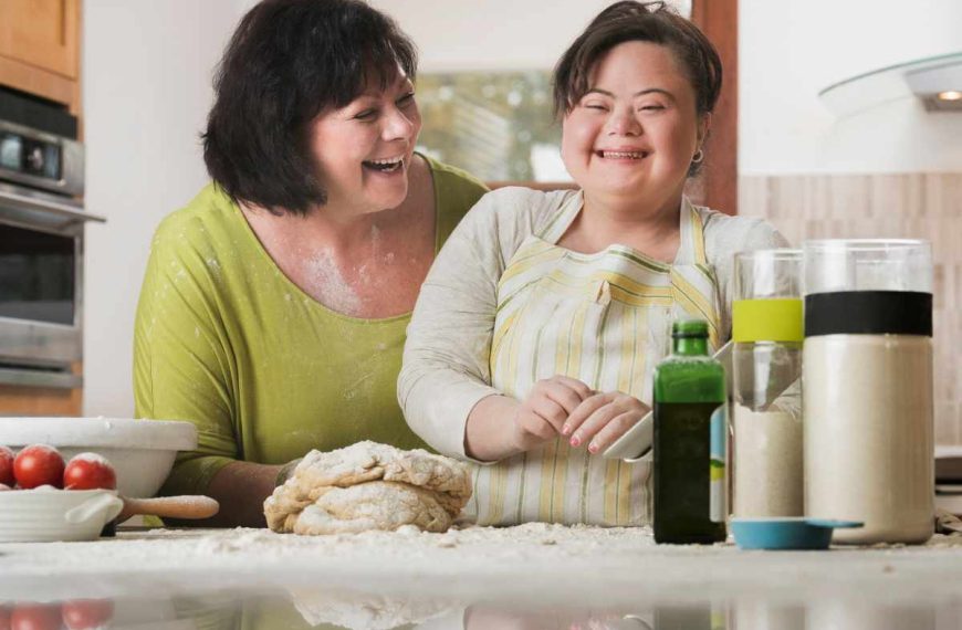 Two women in a kitchen laughing and preparing food.