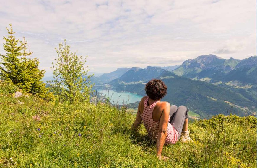 A woman sits on a grassy hill overlooking a lake.