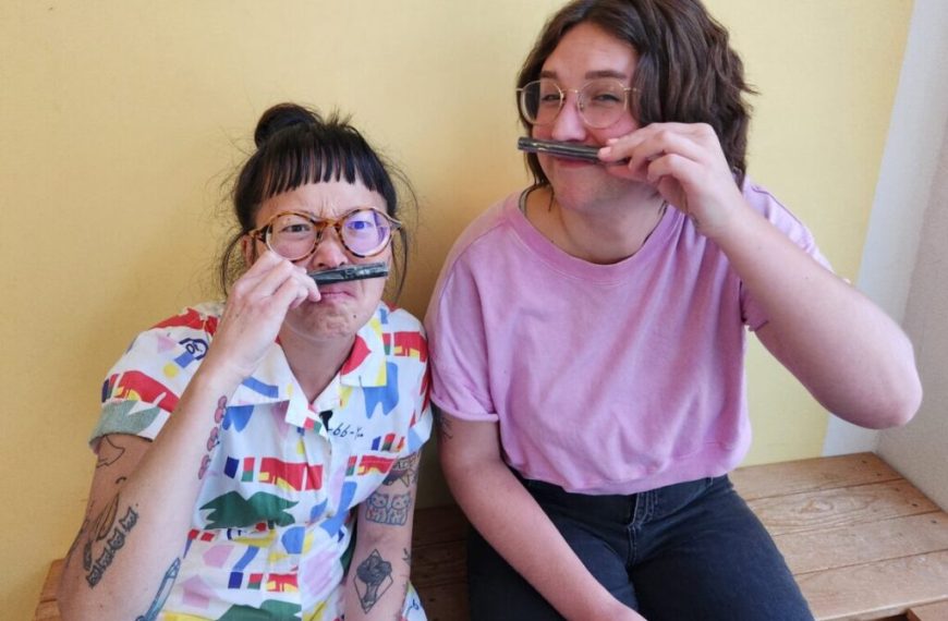 Two women sitting on a bench with their mouths open.