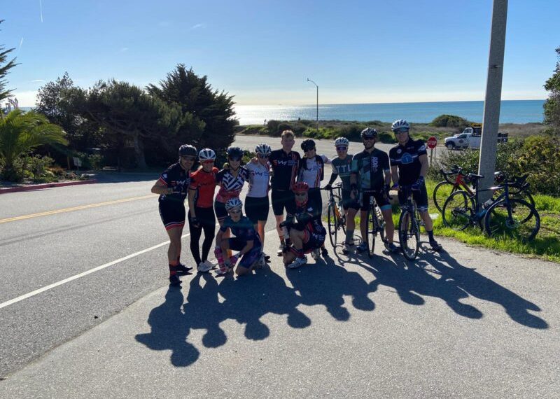A group of cyclists posing for a photo in front of the ocean.