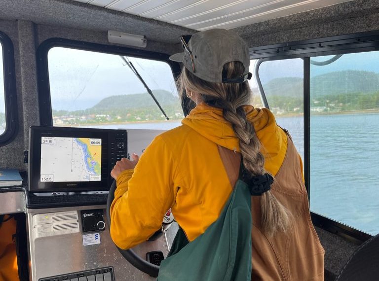 A woman in a yellow jacket is driving a boat.