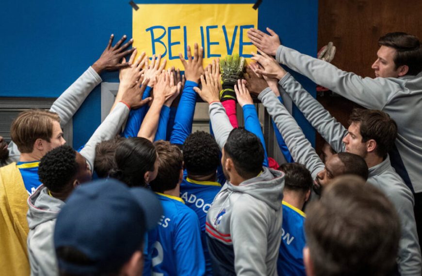A group of soccer players huddle around a sign that says believe.