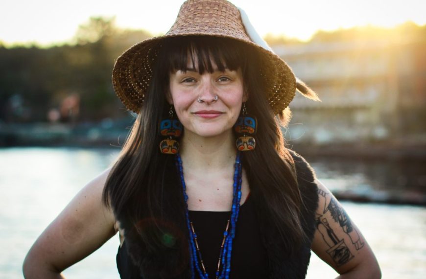 A woman wearing a hat and a straw hat standing by a body of water.