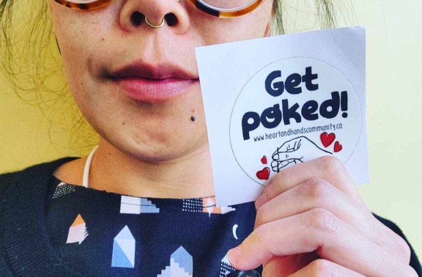 A woman holding up a sticker that says get poked.