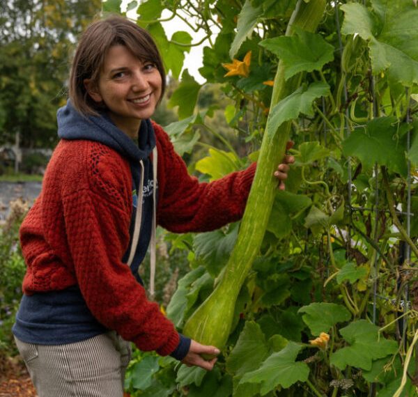 A woman holding a large cucumber.