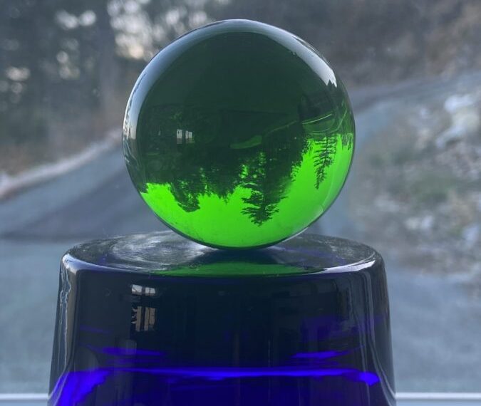 A green glass ball sits on top of a blue vase.