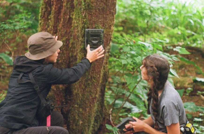 Two people looking at a camera in the woods.