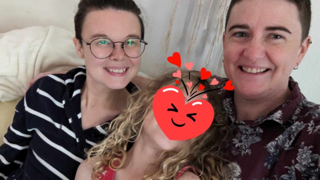 Three people are sitting on a couch with a heart shaped sticker on their faces.