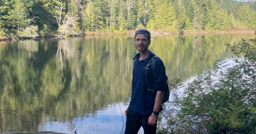 A man enjoying the serenity of a body of water after a long day of hiking.