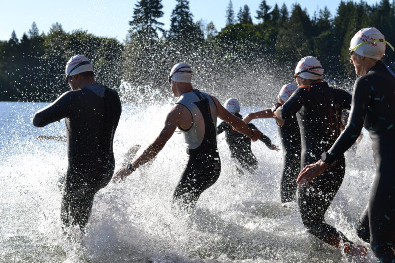 A group of people competing in the Cowichan Challenge, wearing wetsuits and running into the water.