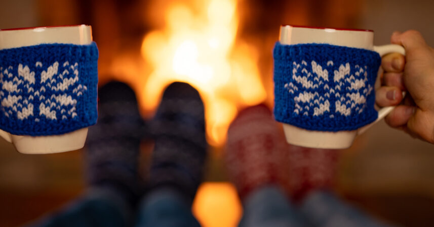 Two people beating the winter blues while holding coffee mugs in front of a fireplace.