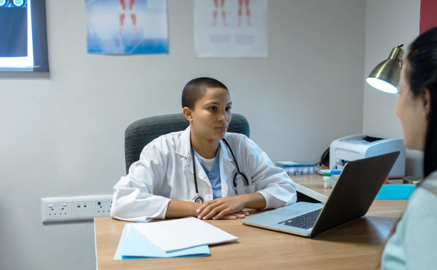 A female doctor is providing healthcare to a patient on a laptop.